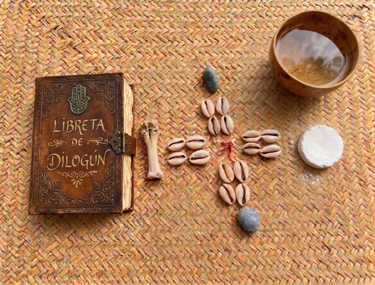 Libreta de Diloggun, caracoles, otá, efún y hueso sobre una estera tejida